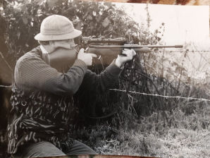  a man out rabbet hunting with his air riffle in  field next to a bush 